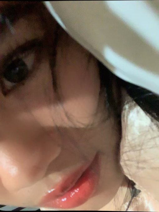 A blurry, low-quality close-up selfie of a person wearing a white hat and glasses, with their face partially obscured.