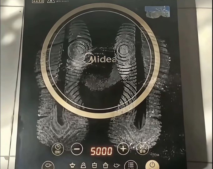 Close-up of a Midea induction cooktop with circular heating zones, control buttons, and a digital display showing the number '5000'.