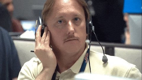A man wearing a headset with a microphone sits at what appears to be a control or trading console, looking off to the side with a slightly distracted expression, embodying the post's joke about crypto traders ($ASTEROID) casually ignoring a small but loud ticker moving on their screens.