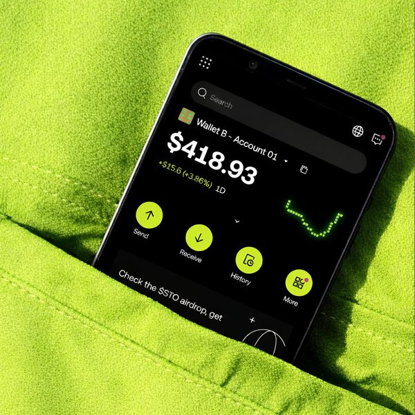 A smartphone rests on a bright green fabric, displaying a crypto wallet app showing "Wallet B - Account 01" with a balance of "$418.93" (+$15.6, +3.86%) alongside Send, Receive, History, and More buttons. The image visually reinforces the caption's message about portable, cross-chain digital money that lives in your pocket rather than traditional vaults.