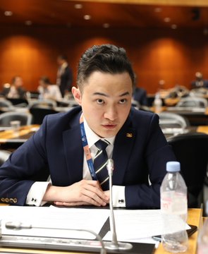 The image shows a man wearing a suit sitting at a desk with a water bottle next to him, possibly during an important meeting or event. The caption reads "Just In: Trump-backed stablecoin USD1 has been delisted by HTX after World Liberty Financial apparently frozeHTX-linked assets, deepening its escalating feud with crypto billionaire Justin Sun." This post is about the recent delisting of a cryptocurrency called Bitcoin Cash from the cryptocurrency exchange Coinbase. It seems that the man in the suit might be involved in or interested in this development.