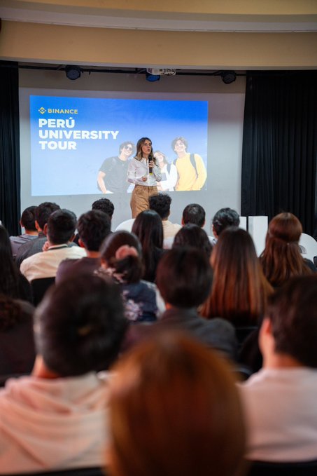 A speaker presents on stage at the Binance University Tour, with a large screen displaying the event's branding behind her, while a packed audience of students listens attentively. The image captures the engaging atmosphere of the session at Universidad La Salle, where attendees learned about Binance's evolving payment solutions and financial ecosystem.