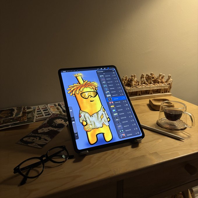 A tablet on a desk displays an Among Us character NFT artwork, accompanied by glasses, a coffee cup, and a Last Supper figurine.