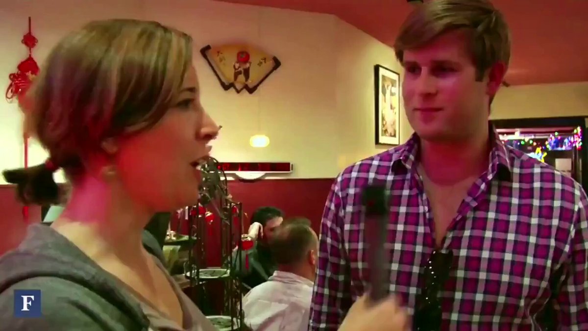 The image shows two people having an animated conversation at a restaurant or cafe. One person appears to be a reporter who has just spent 10 Bitcoin on dinner for the Bitcoin meetup group, while the other person seems to be interested in hearing more about this unique form of currency. The scene takes place in a dining area with tables and chairs, indicating that they are enjoying their meal together.