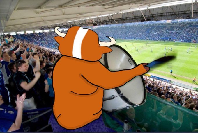 The image features a cartoon depiction of an orange bull with horns, holding a drum while standing at the top of a stadium. The scene takes place during a soccer game, as evidenced by the presence of players on the field. In the background, there is a crowd of people watching the match. A caption in the image reads "SEND EVERYONE WHO EVER SHILLED ZECASH TO PRISON IMMEDIATELY". This message seems to be related to an event or gathering where attendees were encouraged to contribute money for a cause by sending it to a specific address, which is then used to fund a prison sentence.