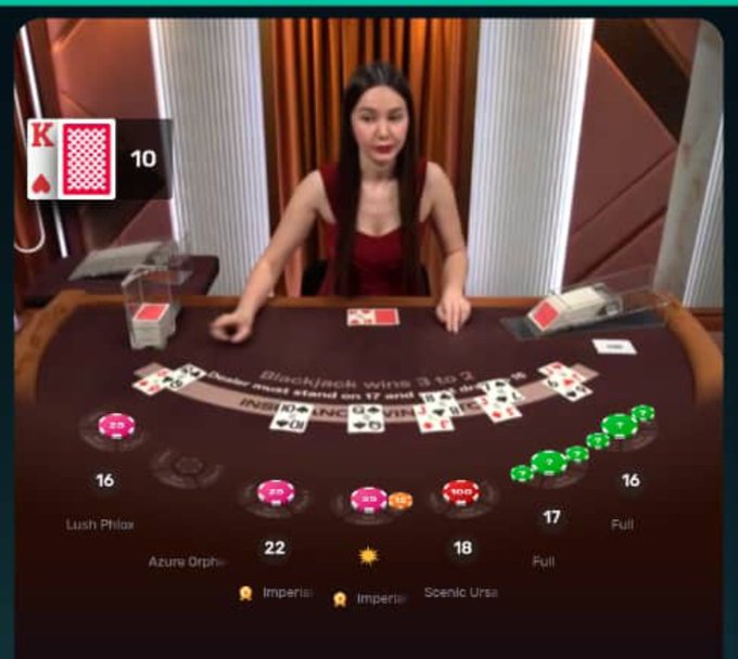A live dealer blackjack stream showing a dealer at a table with player hands displaying scores (16, 17, 22, 18, 16, 17), featuring a King and 10 card displayed in the upper left.