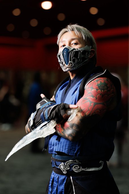A cosplayer dressed as Sub-Zero from Mortal Kombat, wearing a blue ninja outfit, ornate metal mask, and holding a translucent ice blade.