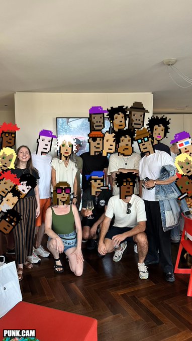 A group photo of people standing and crouching indoors, with pixel-art CryptoPunk avatars digitally overlaid on their faces; the image is watermarked 'PUNK.CAM'.
