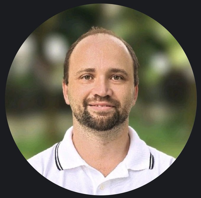 A circular profile photo of a Caucasian man with a beard and receding hairline, wearing a white polo shirt against a blurred outdoor background.