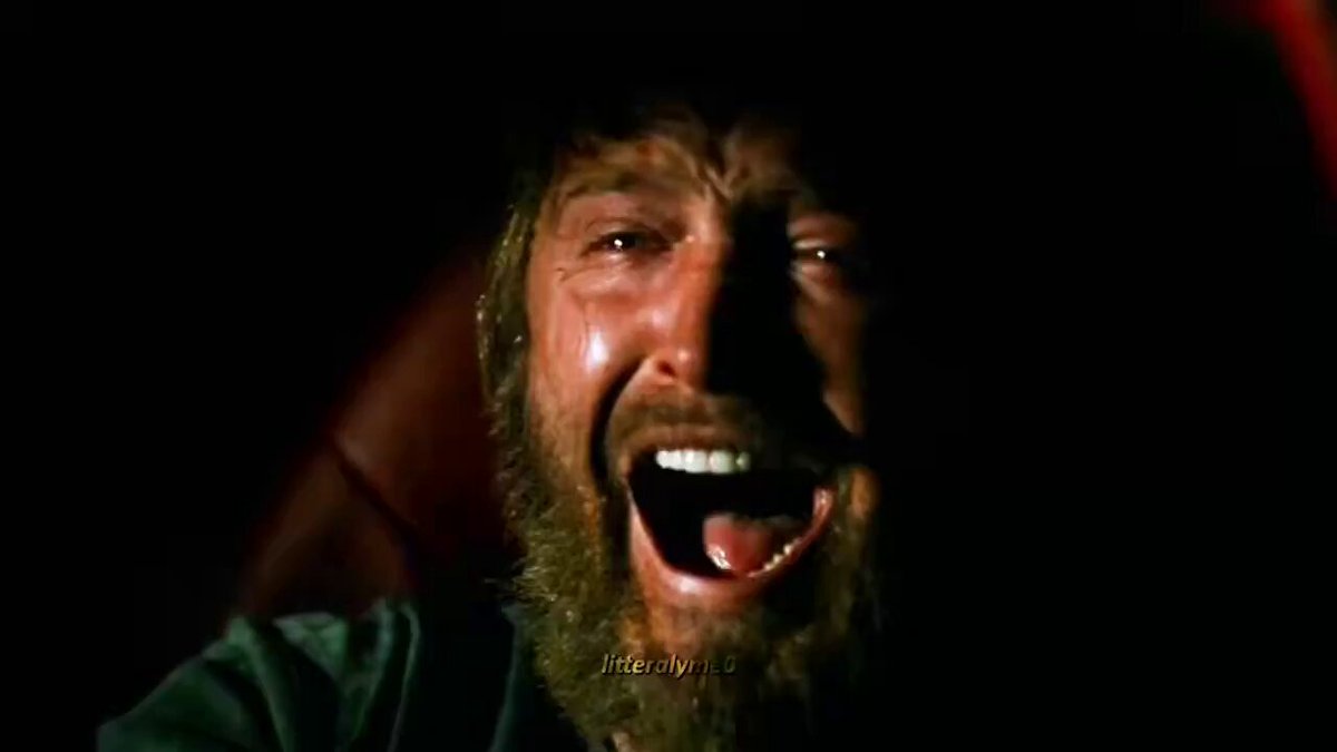 The image shows a man with a beard, wearing a green shirt, laughing heartily while sitting down. The background appears dark, which emphasizes the subject's reaction. There are no texts or other objects visible in the image, making the focus solely on the man and his expression of joy.