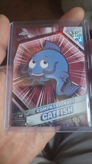 A hand holds a holographic Topps Chrome UFC trading card featuring a cartoon blue fish character named 'Compassionate Catfish'.