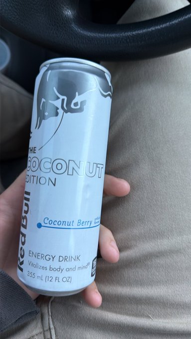 A hand holding a can of Red Bull 'The Coconut Edition' Coconut Berry flavored energy drink inside a car.