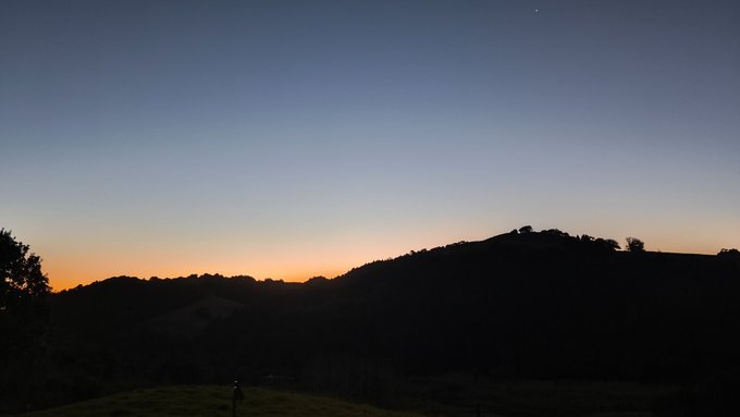 A silhouette of rolling hills and trees is captured against a twilight sky with a gradient of deep blue fading to a warm orange glow at the horizon. The serene evening landscape complements the post's message about earning #B3TR rewards through sustainable laundry practices, evoking the natural beauty that motivates eco-friendly choices.