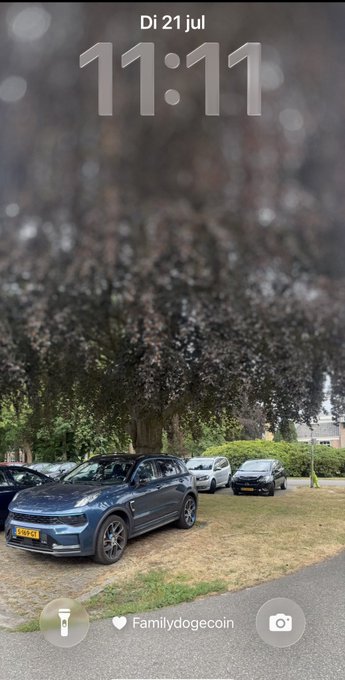 A phone lock screen timestamped 'Di 21 jul 11:11' showing a blue SUV parked under a tree with snow on the ground, with the label 'Familydogecoin' at the bottom.