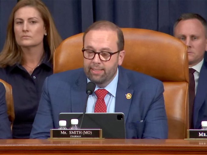 Congressman Mr. Smith (MO), wearing a blue suit and red tie with glasses, sits at a committee chair during what appears to be a congressional hearing.