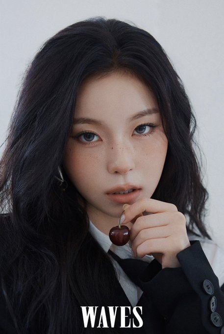 A portrait of a woman with long dark hair and freckles holding a cherry near her mouth, with the word 'WAVES' printed at the bottom.