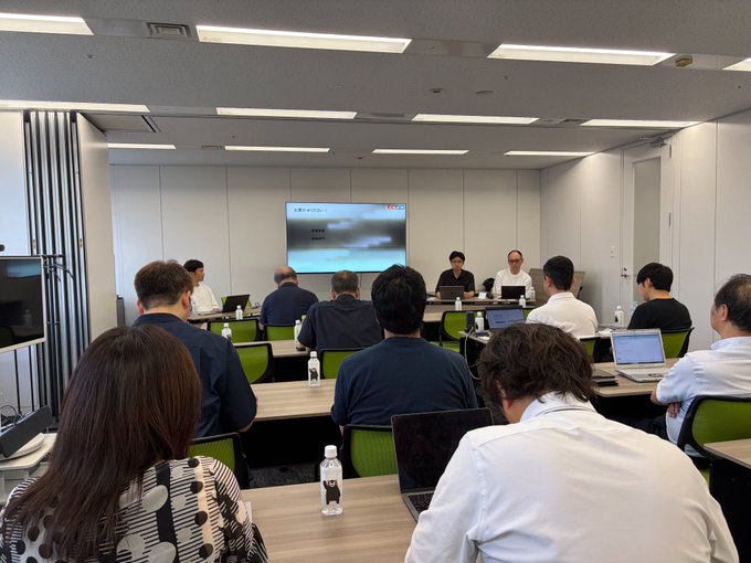 The image shows a meeting room where attendees face a presentation screen displaying Japanese text about "暗号資産" (crypto assets) and "会社" (company), with two presenters seated at the front. This corresponds to the BCCC joint committee session titled "Things to Know Before Your Company Holds Crypto Assets/Stablecoins — Challenges of Accounting and Auditing in Adoption."