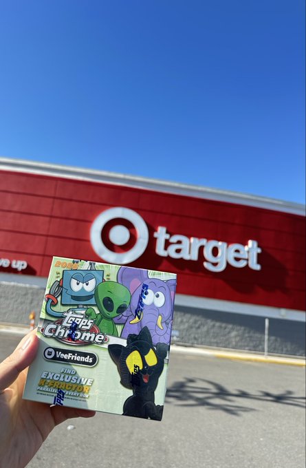 The image features a hand holding up a Target shopping bag that contains a cartoon character sheet of paper. The target logo can be seen behind the person's arm, indicating their location at a Target store. The scene suggests that the person might have purchased some items from the store and is now showing off their new purchase to others or taking a photo for social media.