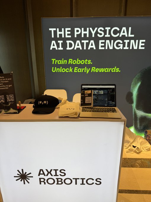 Axis Robotics exhibition booth promoting "THE PHYSICAL AI DATA ENGINE" with the tagline "Train Robots. Unlock Early Rewards," featuring branded merchandise and a laptop.