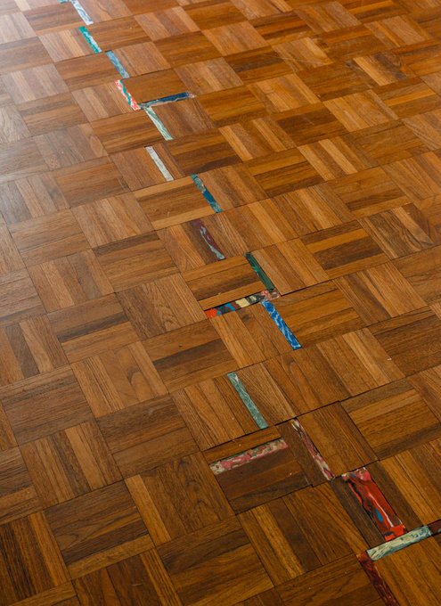 A wooden parquet floor with a distinctive artistic design of colorful inlaid tiles forming an irregular line or crack pattern across the warm-toned wood squares.