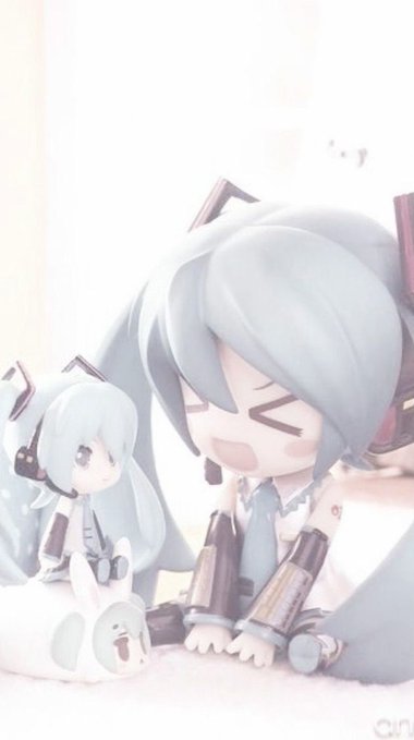 Two Hatsune Miku anime figurines are displayed, with a larger one appearing to laugh joyfully beside a smaller one, set against a soft pastel background.