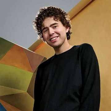 urn with a geometric pattern and a yellow wall backdrop, accompanied by a young man in a black sweater.