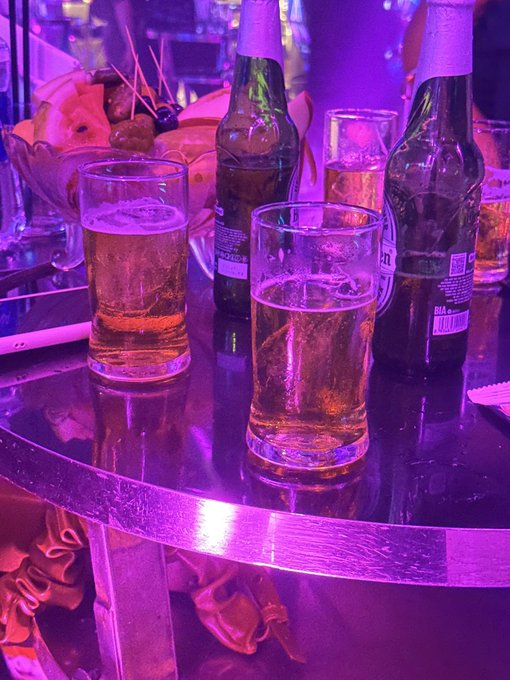 The image shows a table with four glasses of beer, two of which are filled with beer and the other two empty. The glasses are placed next to each other, creating an inviting atmosphere for socializing or enjoying some drinks. The background features purple lights that add a unique ambiance to the scene.
