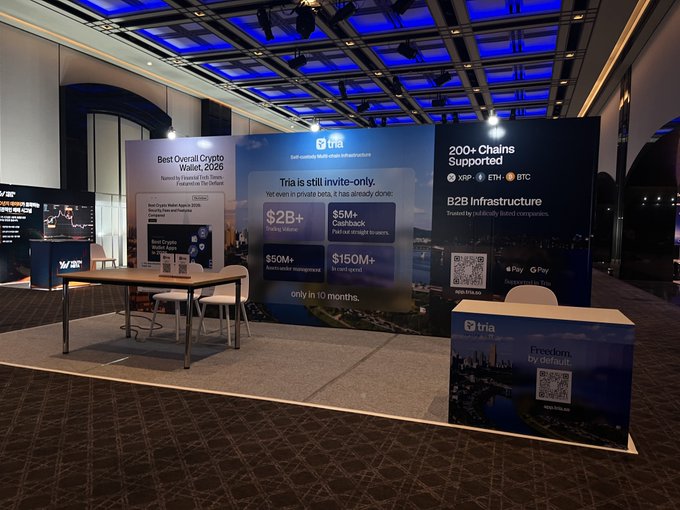 A 'Tria' crypto/Web3 exhibition booth at an event, featuring signage about 'Best Overall Crypto Wallet, 2026', B2B Infrastructure, and various crypto logos including XRP, ETH, and BTC.