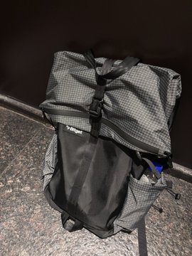 A large gray and black checkered Bliant hiking/travel backpack sitting on a tiled floor against a wall.