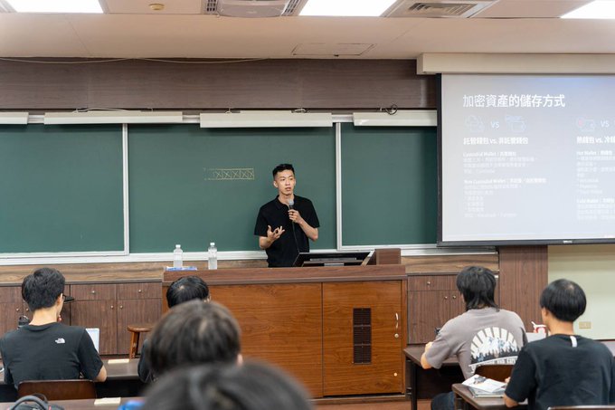 A man gives a presentation in a university lecture hall in front of a green chalkboard and a projected slide about cryptocurrency asset storage methods (加密資產的儲存方式), with students seated in the foreground.