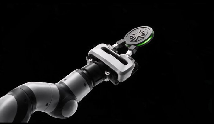 A robotic arm with metallic joints and a circular end-effector featuring a glowing green ring is displayed against a black background.