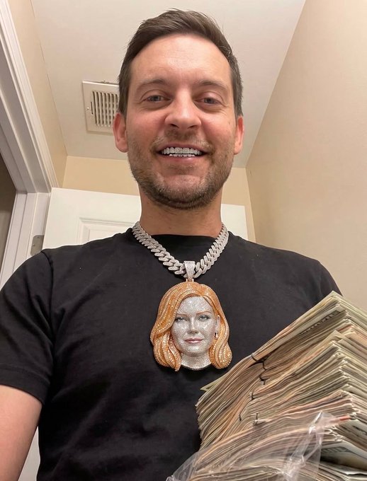 A man smiling while holding a thick stack of cash and wearing a large diamond-encrusted pendant featuring a face design.