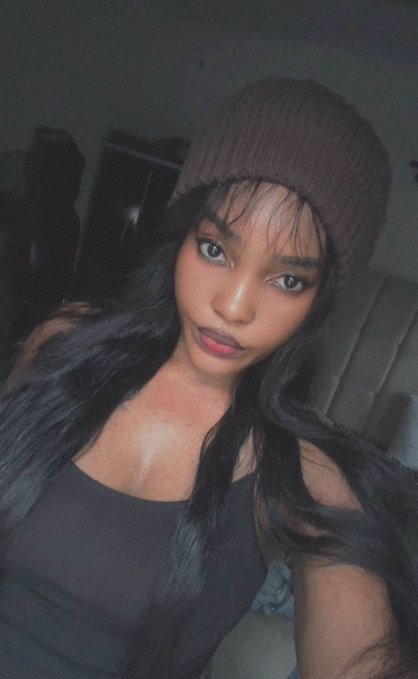 A young woman wearing a brown beanie and a black top takes a selfie in a dimly lit room. The image accompanies a post pleading for an influencer to bless a small African KOL community with a $6,000 $ANSEM allocation, using her striking photo to draw attention to the campaign.