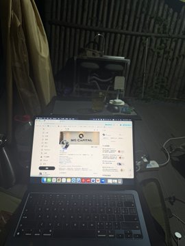 A laptop displays a Twitter/X feed showing a post by Elon Musk while working at a dimly lit café, reportedly by Erhai Lake in Dali, illustrating the nomadic setup of coding during motorcycle travel as described in the post.