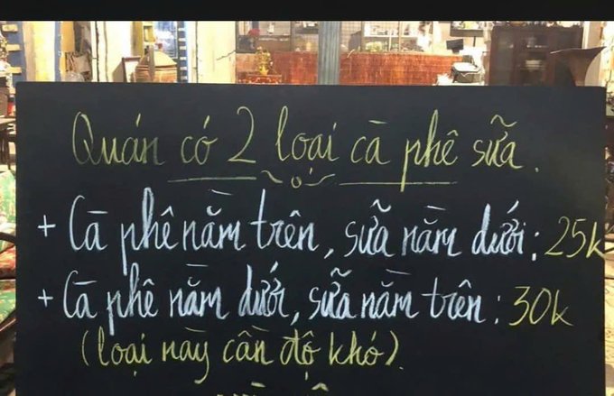 A handwritten Vietnamese chalkboard menu at a coffee shop listing two types of milk coffee: coffee on top, milk below for 25k, and milk on top, coffee below for 30k (this type requires shaking).
