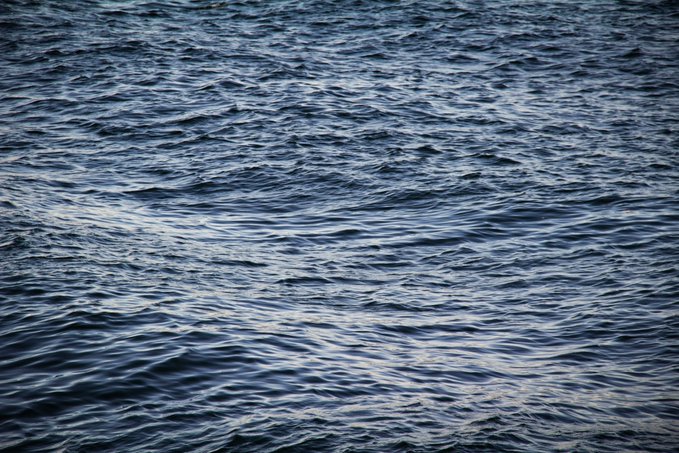 A close-up view of dark blue water with gentle waves and ripples reflecting light across the surface.