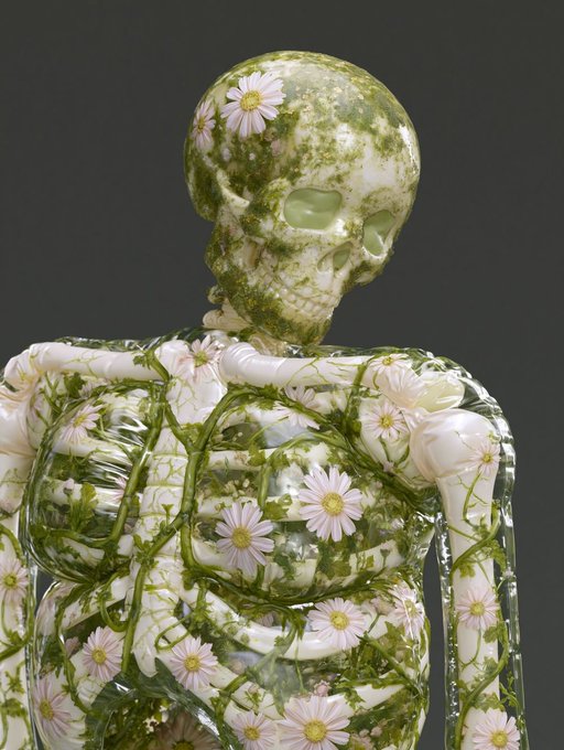 A 3D rendering or sculpture of a translucent anatomical figure containing a skull and ribcage, intertwined with green vines and small pink flowers against a dark background.