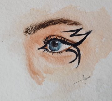 A watercolor painting of a detailed blue eye with dramatic black eyeliner extending into a tribal-like design, signed by the artist "Adriana." The artwork exemplifies the artist's style, which appears to be part of her collection celebrating pieces like "lines" and "A little sunshine" sold to collectors.