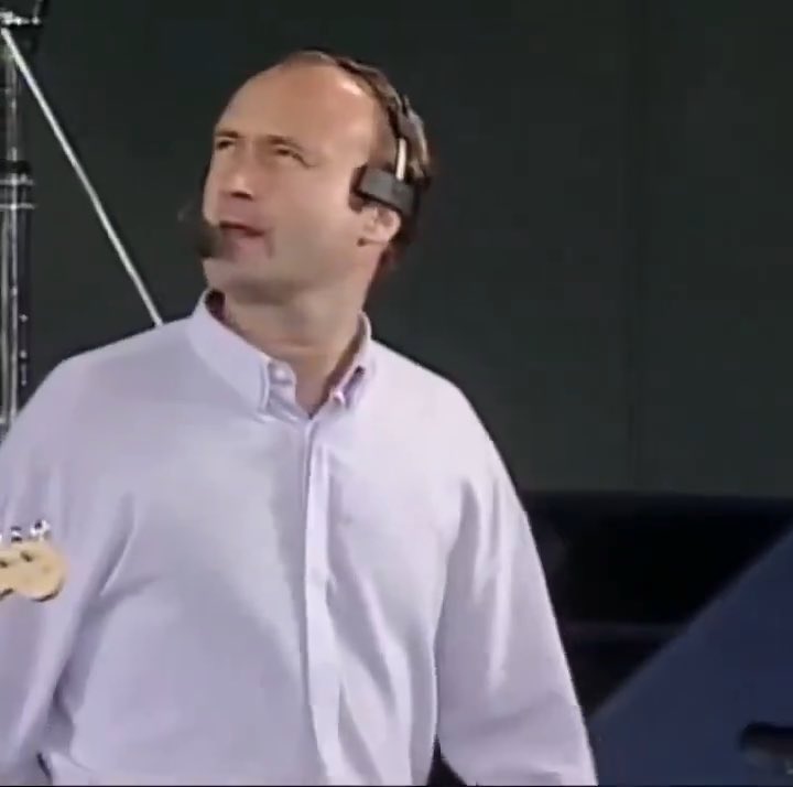 A man wearing a light-colored button-up shirt and a headset microphone, appearing to be speaking or performing at an event.