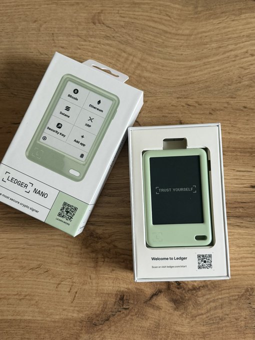 An unboxed Ledger Nano cryptocurrency hardware wallet in mint green, shown next to its packaging with the screen displaying 'TRUST YOURSELF'.