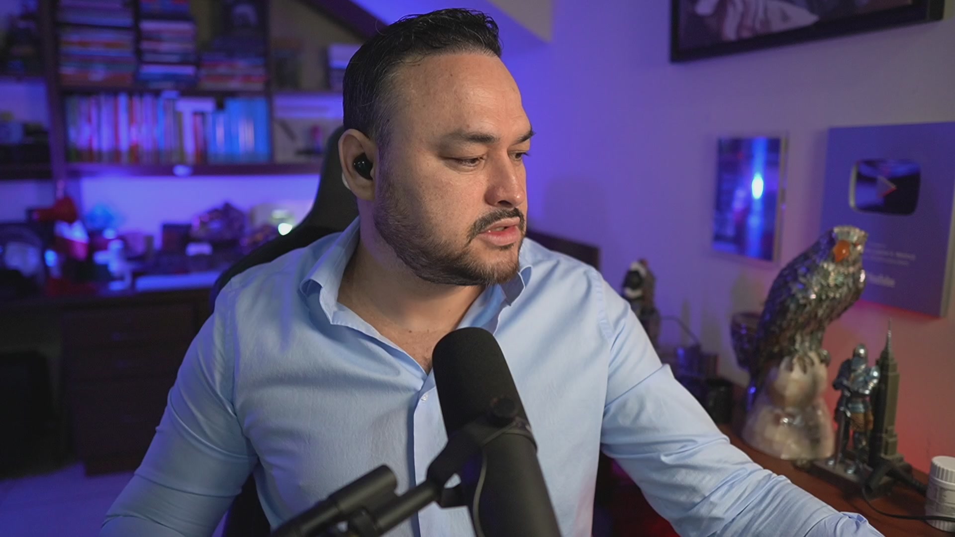 The image features a man wearing a blue shirt, sitting at a desk with a microphone in front of him. The background includes a bookshelf filled with various items such as books and figurines. There are also several books scattered around the room. The caption reads "Esto podría ser el Catalizador que Bitcoin Necesaba", which suggests that there might be some connection between the man's work or hobby involving podcasts, podcasts related to Bitcoin, or a podcast about Bitcoin.