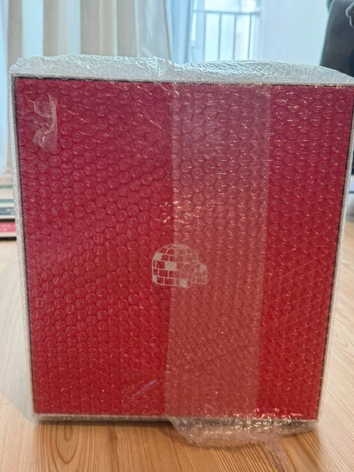 A red Nintendo Switch console box wrapped in clear bubble wrap, sitting on a wooden floor with a window visible in the background.