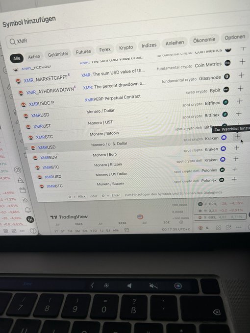 The image shows an open laptop screen displaying a computer monitor with various tabs, including a page about Bitcoin trading views. The monitor has a keyboard located below it, indicating that the user might be actively using the device for work or personal purposes.