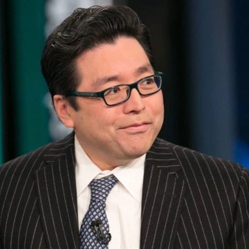 A man with dark hair, glasses, and a pinstripe suit with a patterned tie is shown on what appears to be a TV studio set.