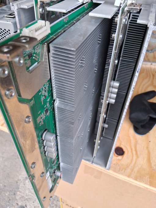 A close-up view of a disassembled electronic device showing a large aluminum heatsink attached to a green printed circuit board, resting on a wooden surface.