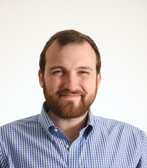 A smiling, balding bearded man in a checkered shirt, pictured against a plain white background. The portrait is presented in the context of a post about Charles Hoskinson releasing an open-source tool called "Anthropies" to strip watermarks from Claude AI outputs.
