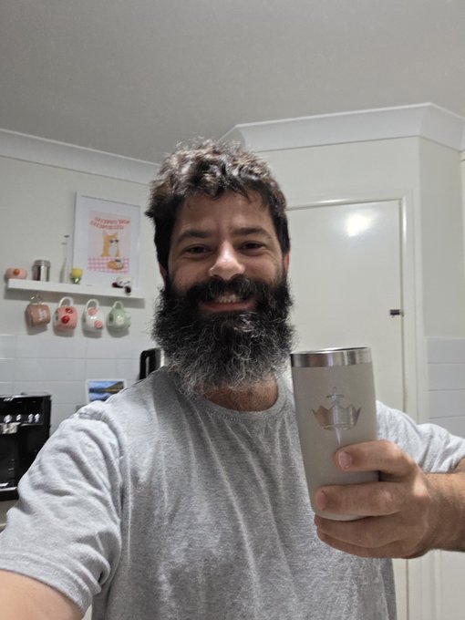 The image features a man with a beard holding a silver cup, possibly containing coffee or tea. The man has a gray t-shirt on and appears to be posing for a photo. In the background, there are several cups and mugs displayed in various positions, suggesting that this could be a kitchen or a similar setting where people gather around a table to enjoy beverages together.

The image also contains text related to investing in the market, which seems unrelated to the man holding the cup. The focus of the image is on the man with the beard and his cup, rather than discussing financial matters.