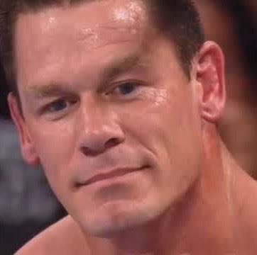 A close-up photo of a young man with short hair, sweating, with a slight smirk, appearing to be in a wrestling or athletic setting.