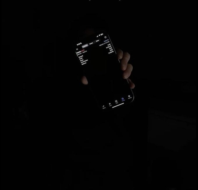 A person holding a smartphone in the dark, with the screen illuminated showing what appears to be a list or message interface.