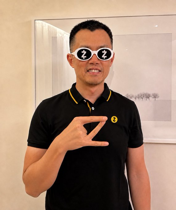 A photo of a smiling man wearing a black polo shirt with yellow trim, with cartoonish white sunglasses and yellow 'Z' emojis edited over his eyes and shirt to make him appear asleep/zoomed out.